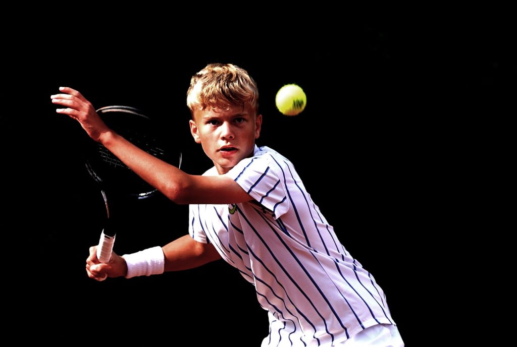 Mladić se priprema udariti tenisku lopticu reketom primjenjujući pravila tenisa