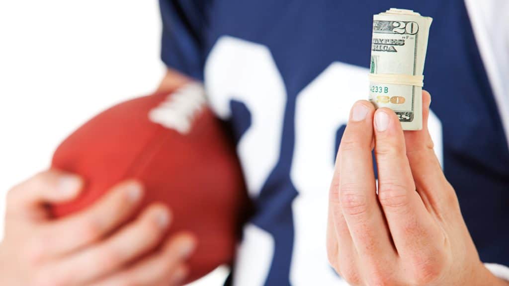 Igrač američkog nogometa drži smotuljak američkih dolara (kako se kladiti na igrače)